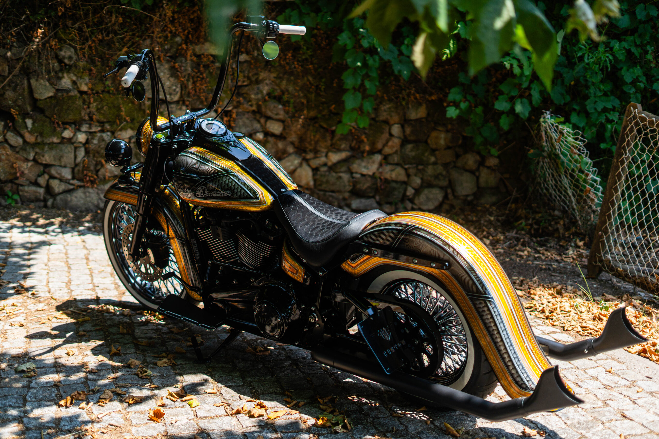 Harley-Davidson Heritage Classic 114 con manillar Ape Hanger y pintura Candy Gold bajo los árboles